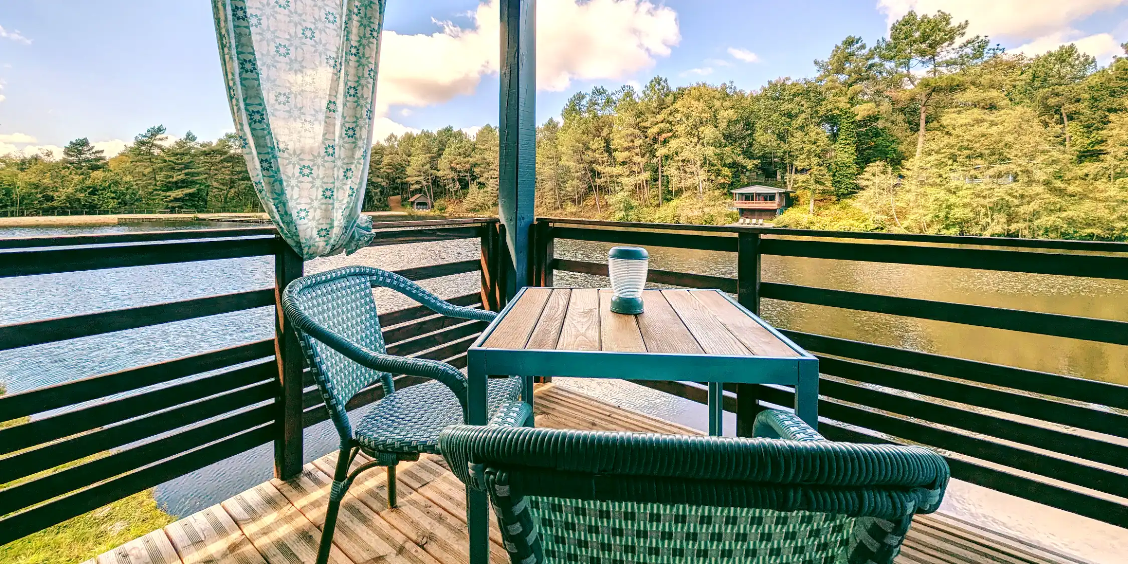 Terrasse en bois couverte du chalet Carpe Sauvage avec vue panoramique sur le lac en Dordogne.